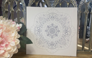 A detailed mandala design on a white canvas, positioned in front of ornate mirror panels, with a bouquet of pink and white flowers to the left, evoking a touch of surrealism.