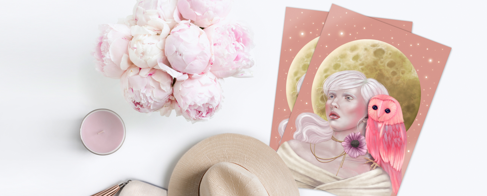 A tranquil workspace with a painting by Melanie Stimmell featuring illustrations of a woman and an owl against a moon backdrop, surrounded by peonies, a candle, and a straw hat on a white