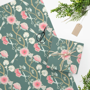 Flat lay of a whimsical floral patterned notebook and a matching Wrapping Paper Craftsman Rose gift-wrapped box, decorated with twine and a blank tag, accompanied by black scissors and a sprig of green leaves.